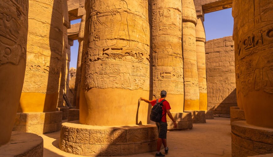 A young tourist walking among the columns with hieroglyphs inside the Karnak Temple